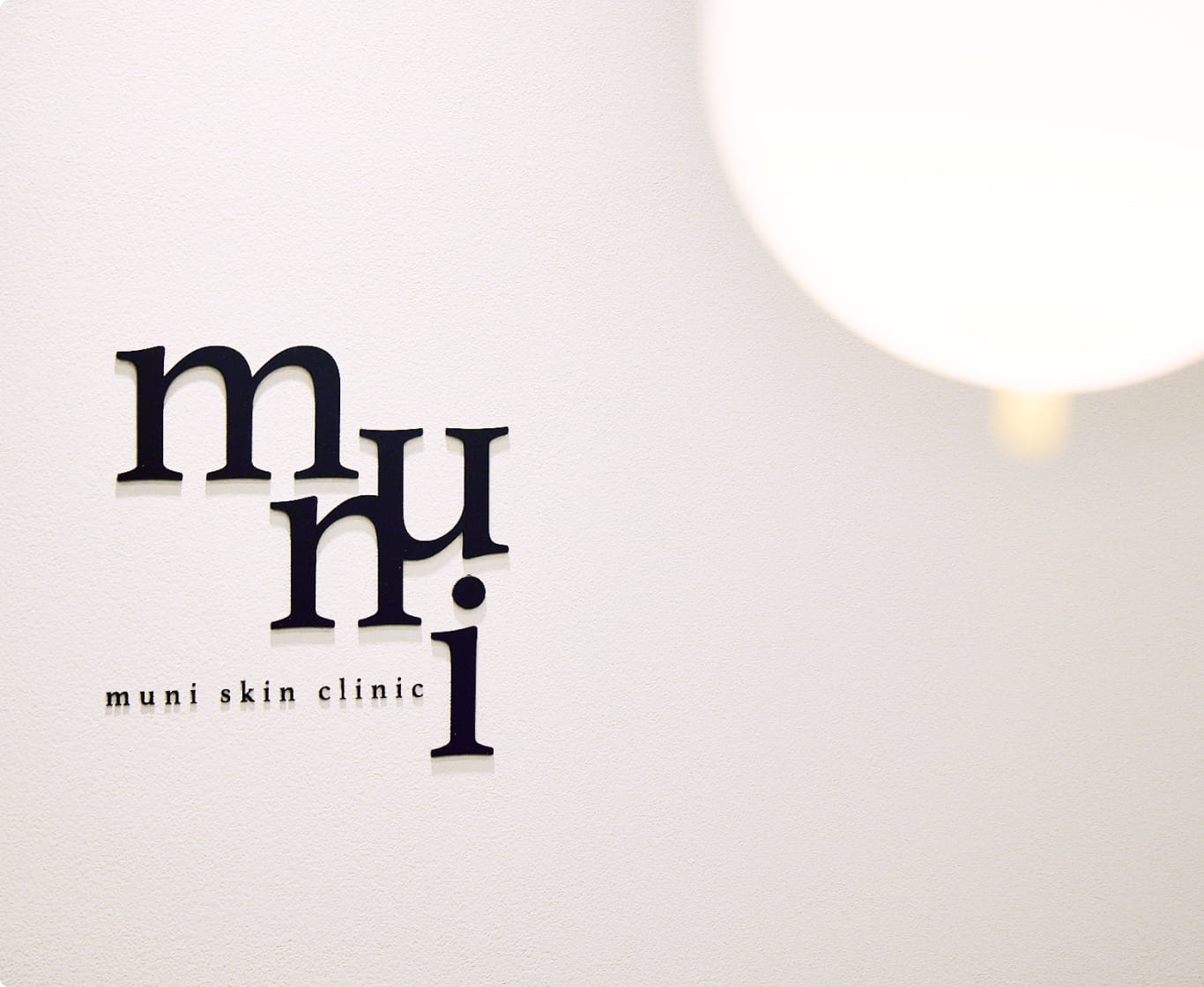 白い壁に「muni skin clinic」のロゴが黒い立体文字でデザインされている